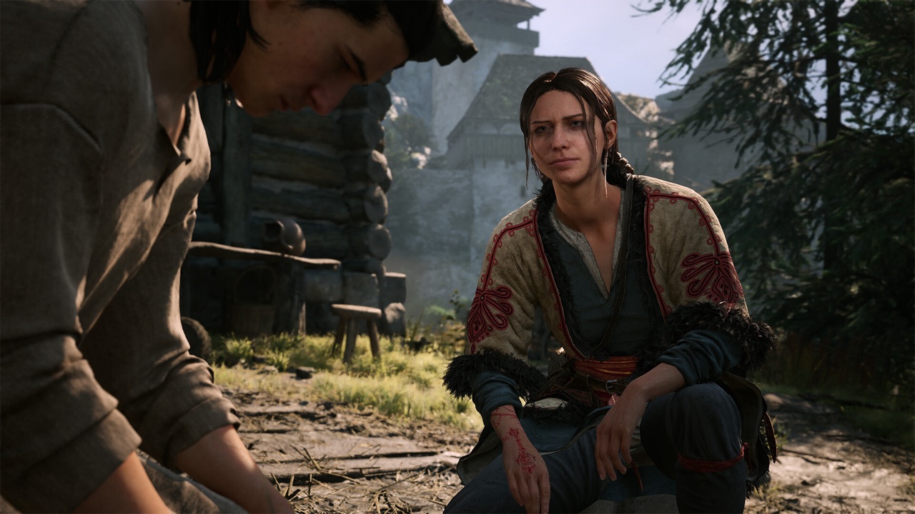 Coen talking with a female character by a well in daylight.